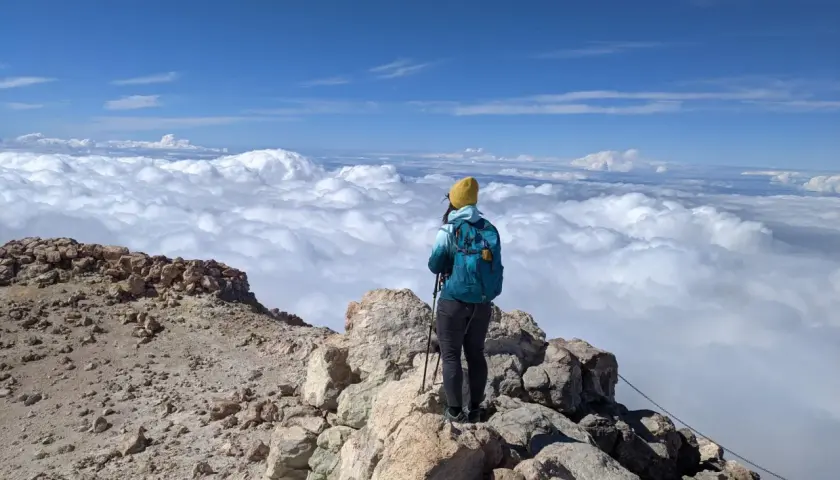 Widok z góry na chmury, osoba z plecakiem i kijkami trekkingowymi na skalistym szczycie. To wspaniałe wejście na Teide!