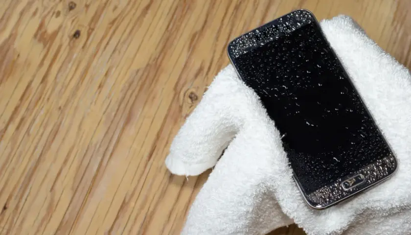 Telefon Samsung z kroplami wody na ekranie, owinięty w biały ręcznik. Jak wyłączyć czujnik wilgoci Samsung, gdy telefon jest mokry?