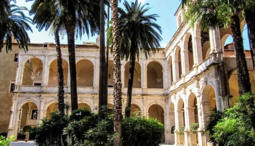Cour intérieure avec palmiers, arcades et balcons, évoquant le Vittoriano et le Palazzo Venezia.