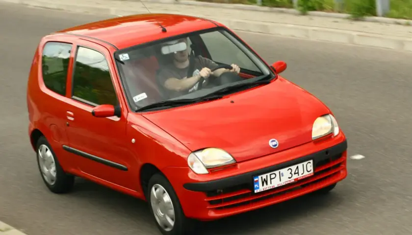 Czerwone Fiat Seicento w ruchu drogowym, widok z przodu i z boku.