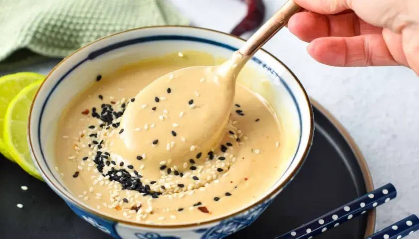 A creamy tahini dressing, sprinkled with black and white sesame seeds, is scooped from a bowl. This tahini sauce is a delicious alternative to miso for many dishes.
