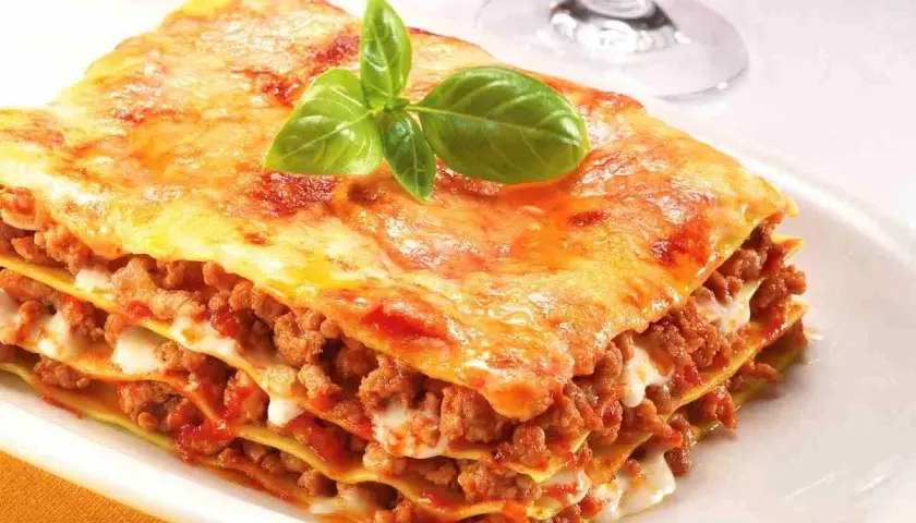 Porzione di lasagne fatte in casa, stratificate con ragù e besciamella, guarnite con basilico fresco.
