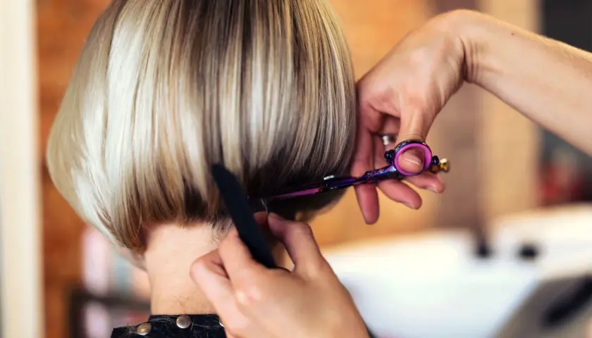 Fryzjerka precyzyjnie modeluje prosty bob, używając kolorowych nożyczek.