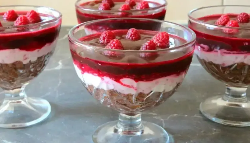 Pyszny deser z mascarpone i galaretką malinową, udekorowany świeżymi malinami, podany w eleganckich pucharkach.