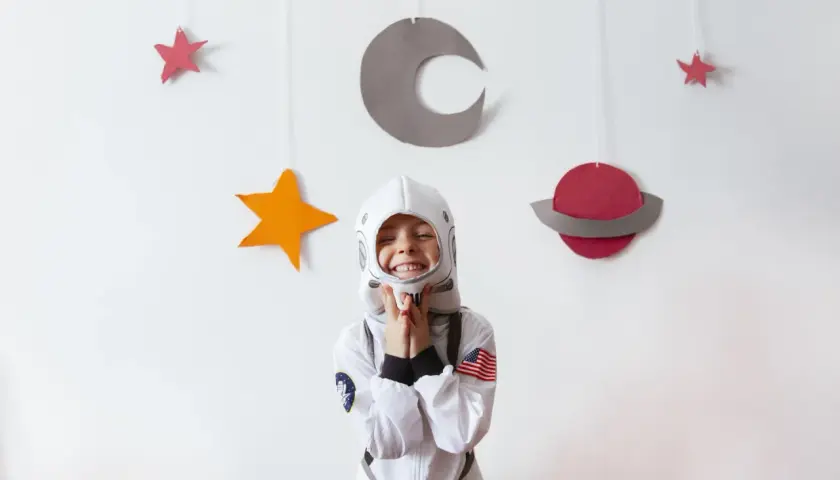 Uśmiechnięte dziecko w stroju astronauty na tle kosmicznych dekoracji.