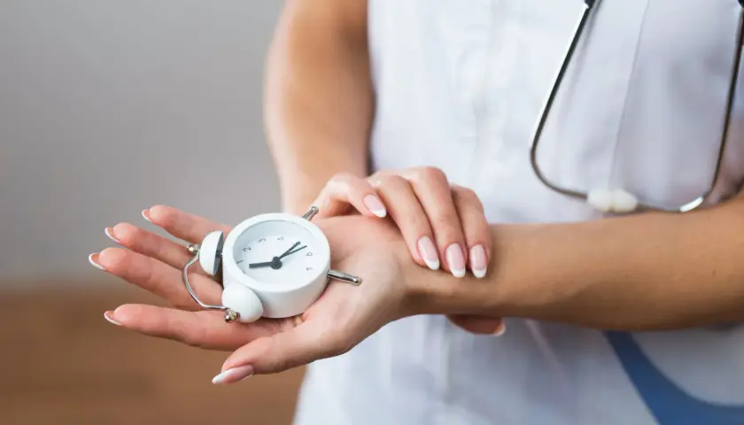 Manos de profesional de la salud sostienen un reloj despertador, simbolizando la presión de trabajo y la importancia del tiempo en la atención médica.