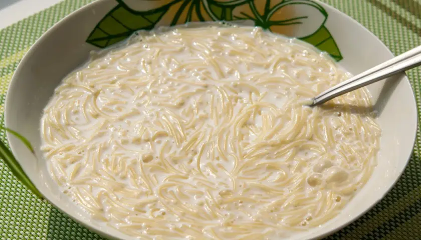 Zupa mleczna z makaronem, podana w misce z motywem kwiatowym. Widoczna łyżeczka zanurzona w kremowym daniu.