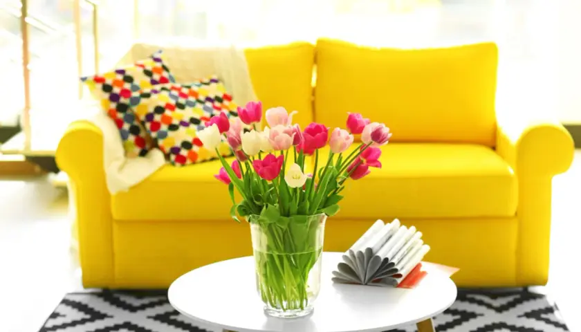 Ein gelbes Sofa mit bunten Kissen und Tulpen auf einem Beistelltisch. Diese stilvolle Deko im Wohnzimmer strahlt Fröhlichkeit aus.