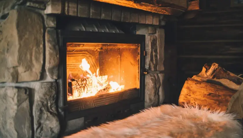 Un feu crépite joyeusement dans une cheminée en pierre, réchauffant l'atmosphère d'un chalet rustique. Des bûches attendent patiemment à côté.