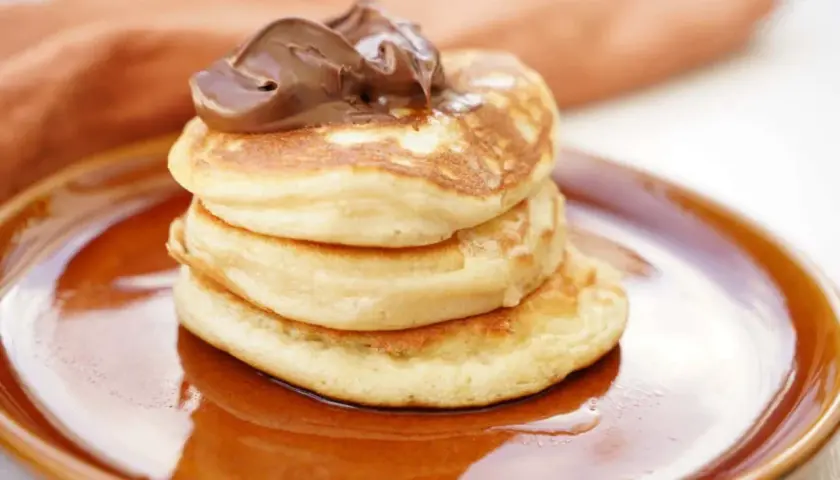 En stapel fluffiga amerikanska pannkakor toppas med chokladkräm på en brun tallrik.