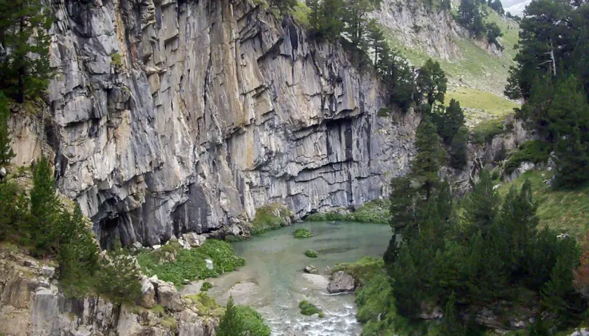 Impresionante pared rocosa junto a un río y vegetación exuberante en el forau de Aigualluts.