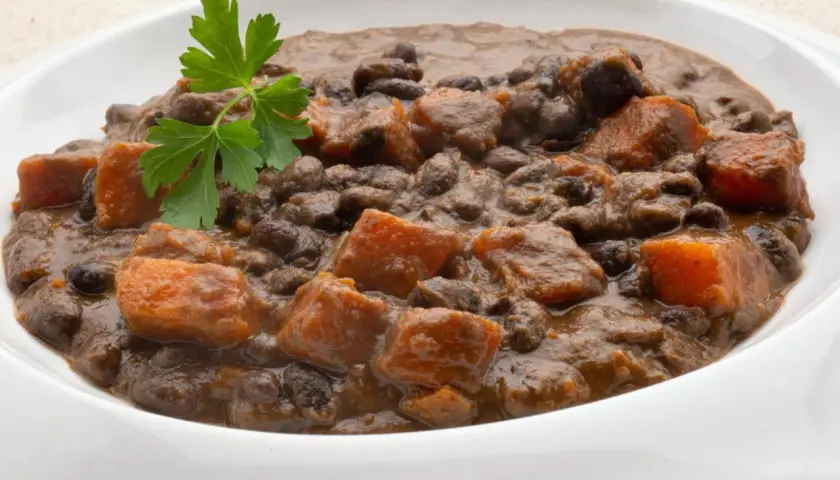 Un plato de frijoles negros con trozos de camote y perejil fresco.
