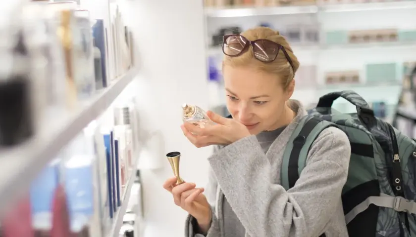 Kobieta z plecakiem wącha perfumy, zastanawiając się, ile kosztują perfumy na lotnisku.