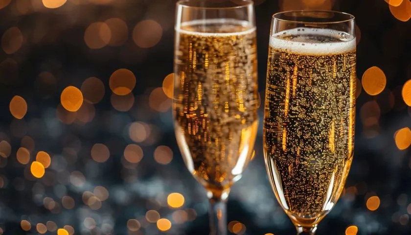Dwa kieliszki musującego prosecco, pełne bąbelków, na tle rozmytych, złotych świateł. Czy prosecco to szampan? To pytanie często zadawane przy takich okazjach.