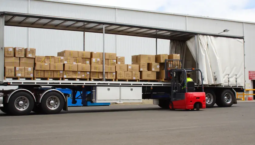 Czerwony wózek widłowy ładuje pudła na naczepę. Taki tir może przewieźć nawet 25 ton ładunku.