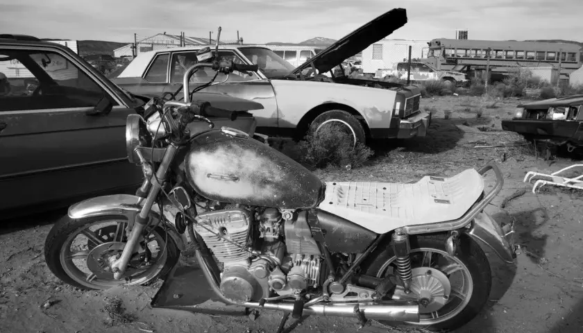 Una moto vieja y un coche en un desguace. ¿Como saber si una moto esta dada de baja? Busca señales de óxido y piezas faltantes.