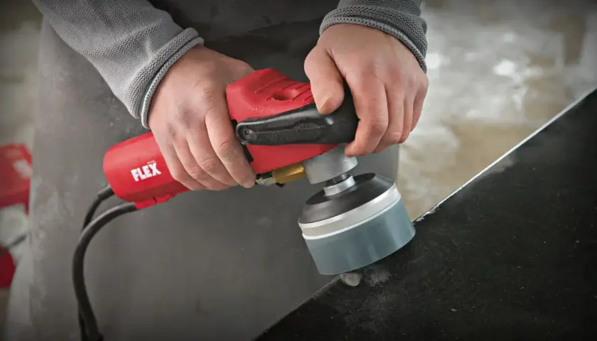 Präzises Stein schleifen mit einem roten Winkelschleifer von Flex. Staub wirbelt auf, während die Kante bearbeitet wird.