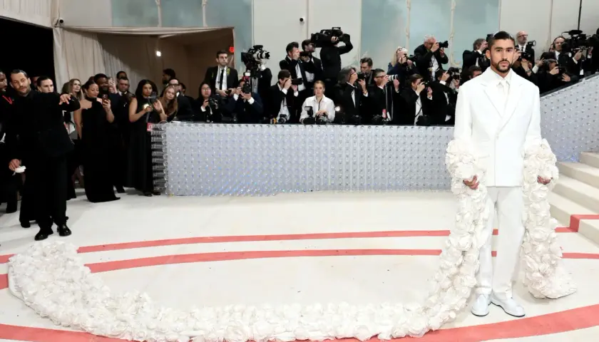 Bad Bunny deslumbra en la Met Gala con un traje blanco adornado con flores, rodeado de fotógrafos.