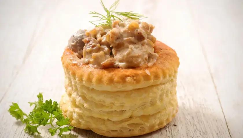 Une délicieuse bouchée à la reine, garnie d'une sauce crémeuse aux champignons et volaille, sur fond de bois clair.