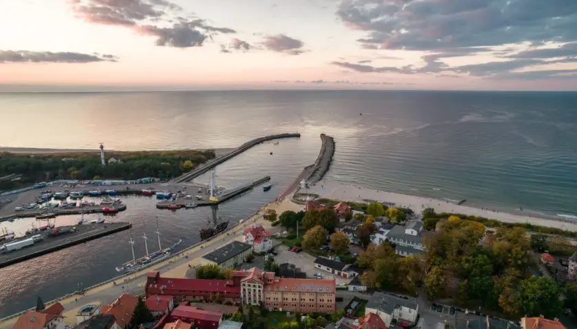 Widok z lotu ptaka na port i plażę w Ustce. Widać łodzie, latarnię morską i budynki. To jedne z wielu ustka atrakcje turystyczne.