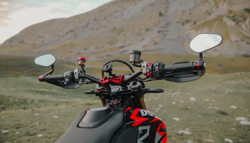 Manubrio di una moto con specchietti bar end, pronto per un'avventura tra le montagne.