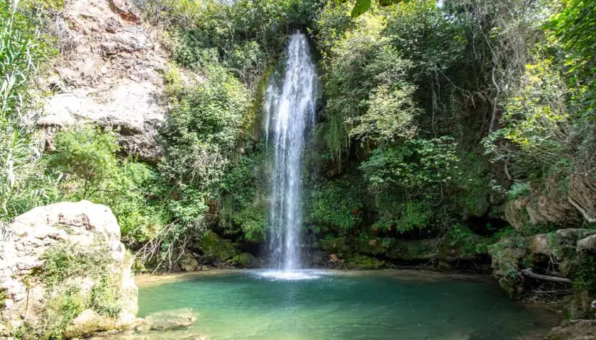 Los chorradores de Navarres, una cascada cae en una poza de agua turquesa rodeada de vegetación exuberante y rocas.