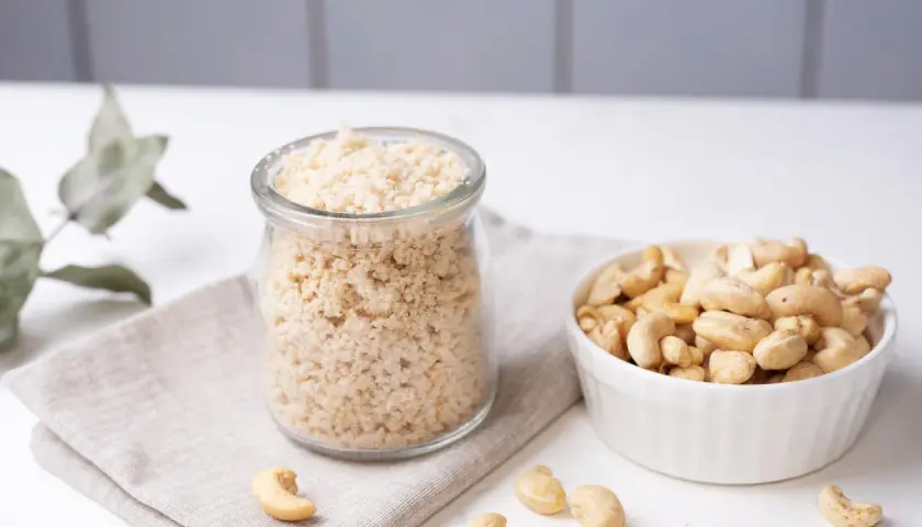 Zutaten für veganen Parmesan selber machen: Cashewkerne in einer Schüssel und fertig gemahlene Masse in einem Glas.