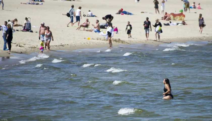 Plaża pełna ludzi, a w wodzie kąpie się kobieta. Warto sprawdzić, ile stopni ma Bałtyk latem, by móc cieszyć się takimi widokami.