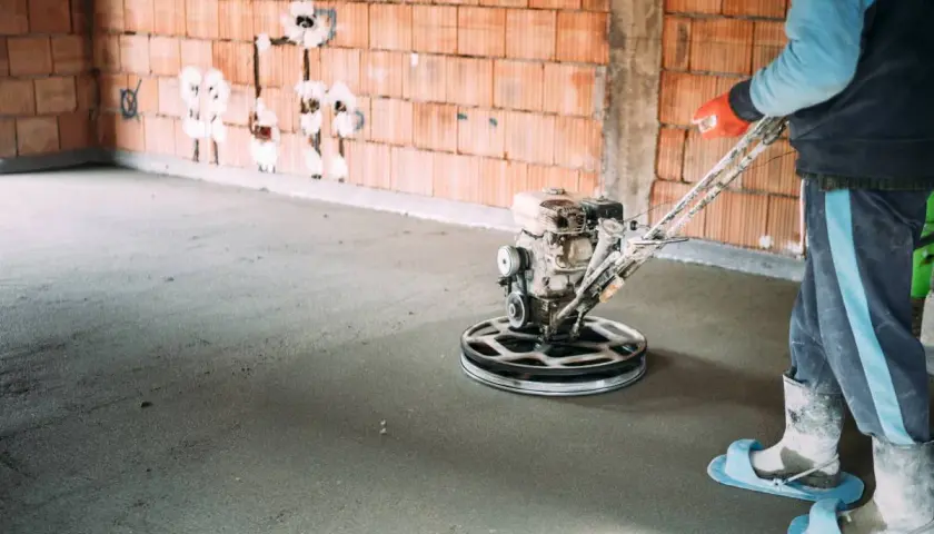 Pracownik wykonuje zacieranie betonu za pomocą mechanicznej zacieraczki.