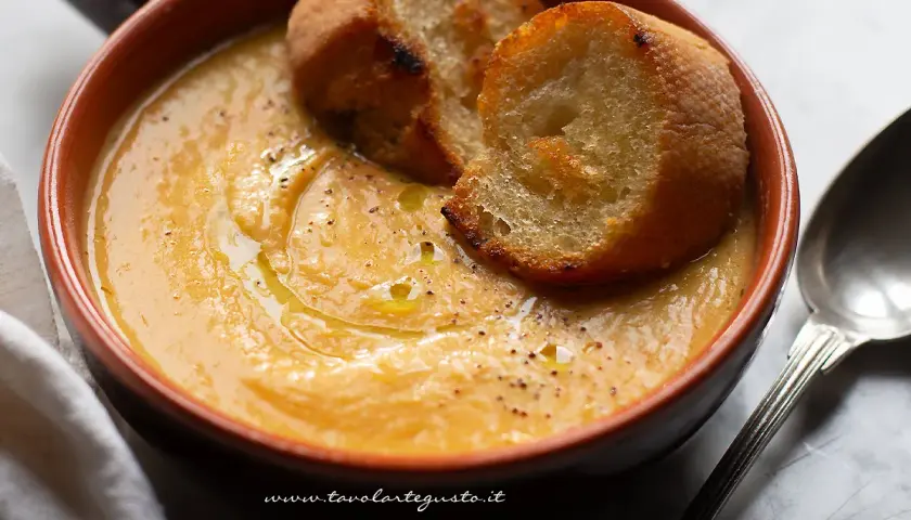 Una ciotola di terracotta contiene una vellutata crema di fagioli cannellini, guarnita con crostini dorati e un filo d'olio.