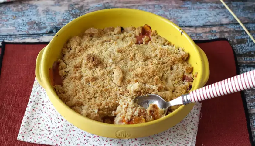 Un délicieux crumble abricot tout juste sorti du four, prêt à être dégusté. La cuillère y a déjà fait un trou.