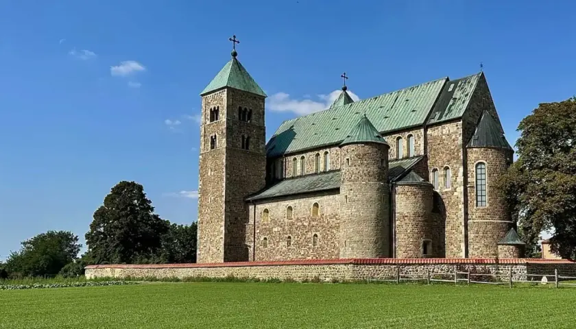 Romańska bazylika tum pod Łęczycą, z zielonymi dachami i kamiennym murem, na tle błękitnego nieba.