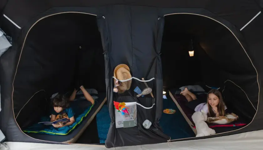 Dzieci cieszą się **campingiem dla dzieci** w namiocie. Chłopiec czyta książkę, dziewczynka bawi się z pluszakiem.
