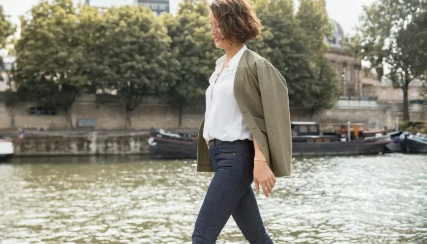 Une femme élégante à Paris, parfaite pour savoir comment s'habiller quand il fait 10 degrés femme : jean, chemise blanche et veste kaki.