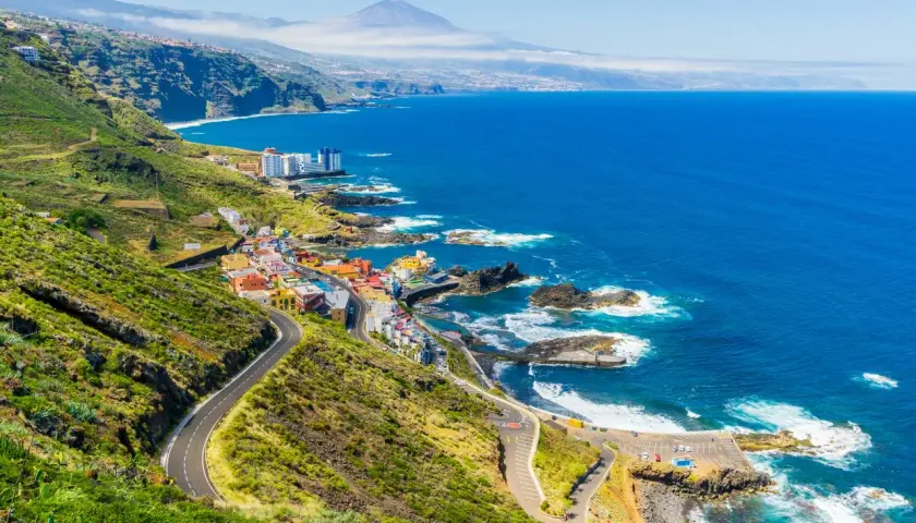 Costa de Tenerife con pueblo colorido, mar azul y el Teide al fondo. ¡Perfecto para tus viajes a Tenerife todo incluido 2x1!