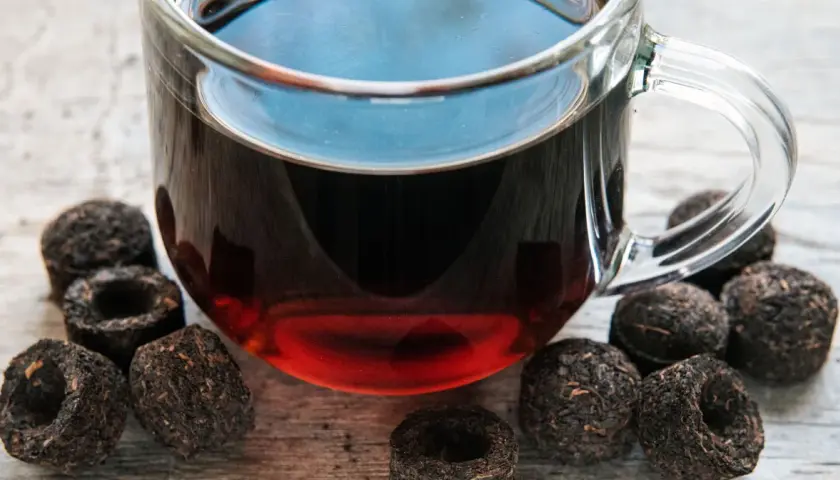 Szklanka z aromatycznym, czerwonym herbatą, otoczona sprasowanymi liśćmi, gotowa do zaparzenia.