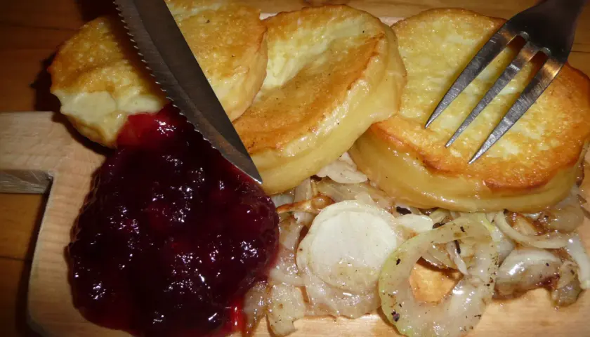 Usmażony oscypek z żurawiną, cebulą i sztućcami na desce.