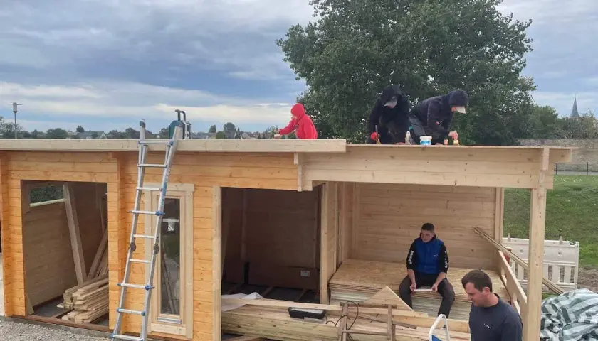 Arbeiter erneuern das **Gartenhaus Dach**. Eine Leiter steht bereit, während mehrere Personen auf dem Dach arbeiten.