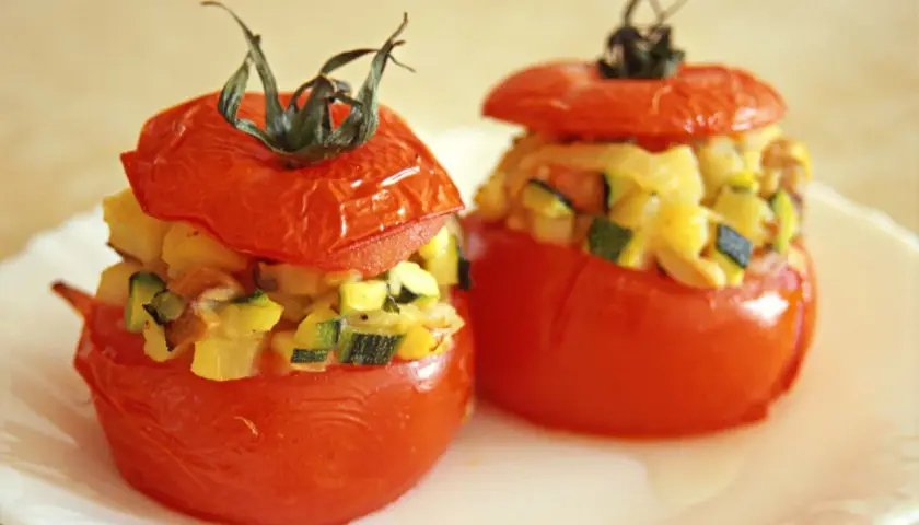 Deux tomates farcies végétariennes garnies de légumes coupés en dés, servies sur une assiette blanche.