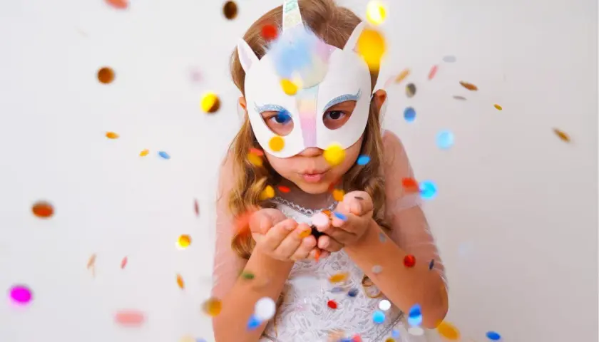 Ein Mädchen mit Einhorn-Faschingsmaske bläst Konfetti. Eine tolle Vorlage für deine nächste Party!
