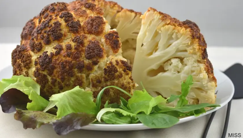 Coliflor al horno, dorada y tierna, servida con una fresca ensalada verde. Un plato saludable y delicioso.