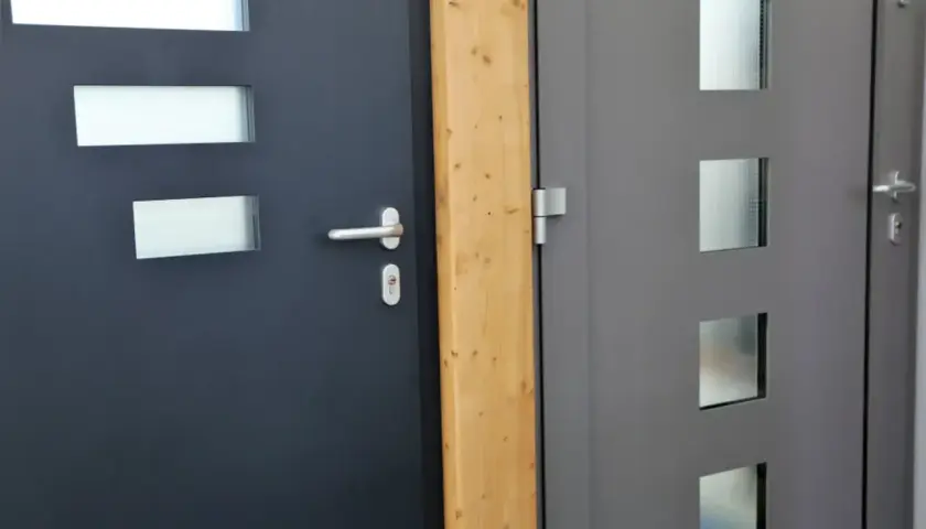 Dwa nowoczesne drzwi wejściowe, ciemnoszare i szare, z przeszkleniami. Dowiedz się, jak uszczelnić drzwi wejściowe, by chronić dom.