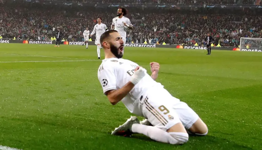 Karim Benzema świętuje zwycięstwo w Lidze Mistrzów, klęcząc na boisku w białej koszulce Realu Madryt.