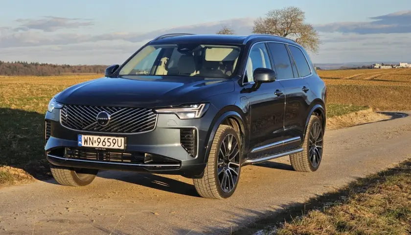 Ciemnoszary Volvo XC90 T8 na tle jesiennego krajobrazu. Elegancki SUV z nowoczesnym grillem i światłami LED.