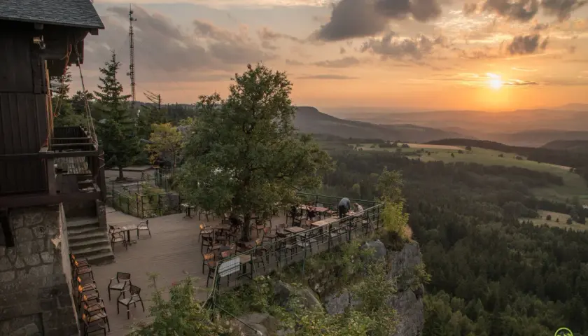 Widok z tarasu restauracji na Górach Stołowych o zachodzie słońca. Drewniany taras z meblami, otoczony skalistym zboczem i lasem.