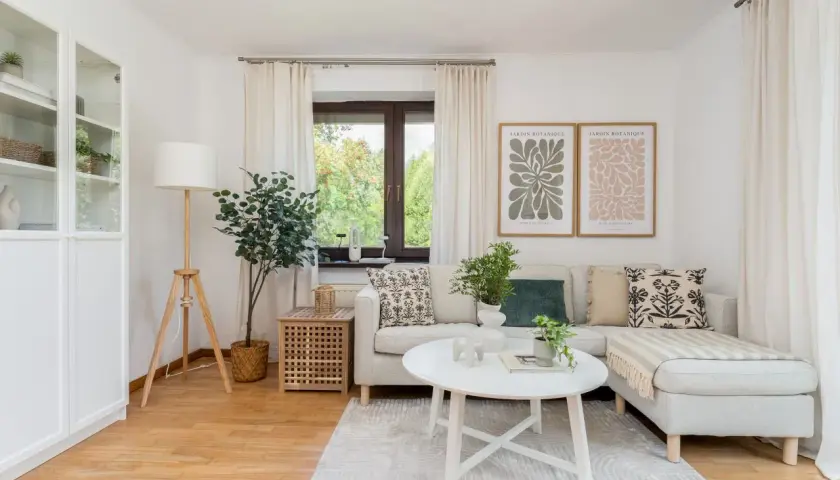 Przytulny salon, idealne **mieszkanie dla młodych**. Jasna sofa, stolik kawowy, rośliny i botaniczne plakaty tworzą relaksującą atmosferę.