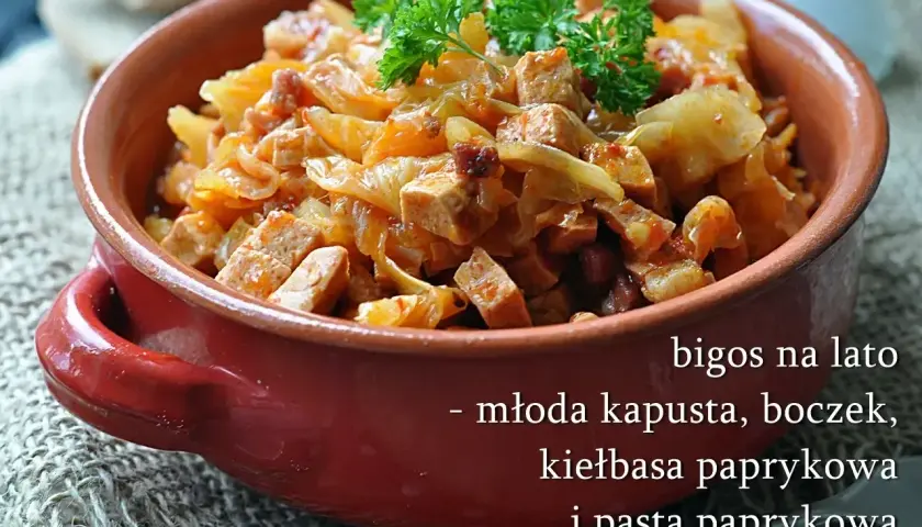 Pyszny bigos z młodej kapusty z boczkiem i kiełbasą paprykową, podany w glinianym naczyniu, udekorowany natką pietruszki.
