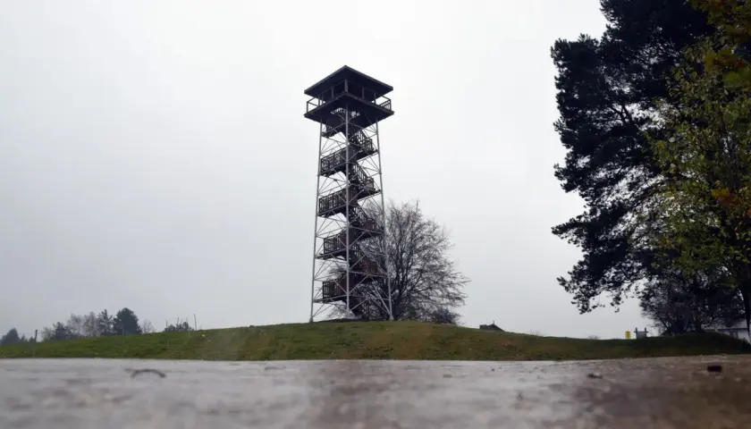 Wieża widokowa na górze lemana, z krętymi schodami i drewnianymi platformami, góruje nad zielonym wzgórzem.