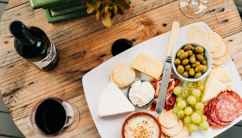 Un plateau de fromages variés, charcuterie, olives et raisins, accompagné d'une bouteille et d'un verre de vin rouge. Quel vin rouge avec un plateau de fromage varié ?