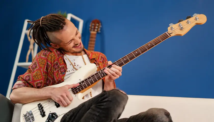 Mężczyzna z dredami gra na białej gitarze basowej. Ile strun ma gitara basowa? Ta ma cztery.